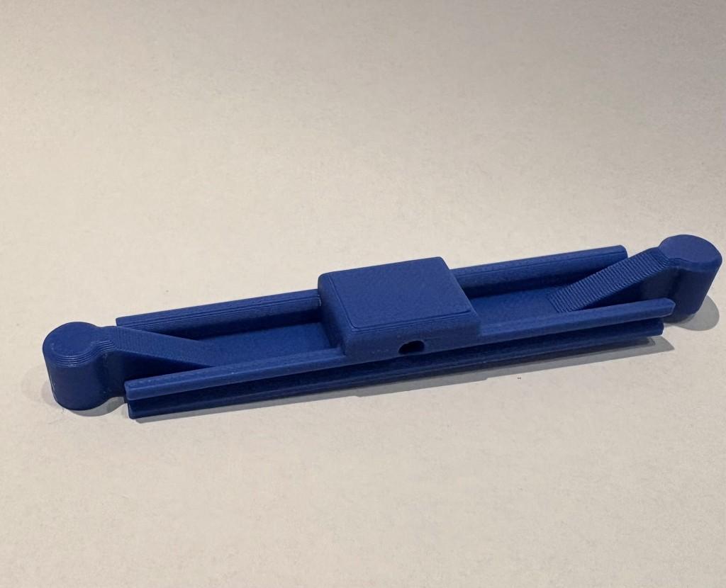 Diepblauw 3D-geprint basisconnector-element: symmetrisch brugstuk met centraal rechthoekig blok en gaatje, twee armen met U-vormige rails en diagonale verstijvers, cilindrische penaansluitingen aan de uiteinden, op een lichte ondergrond