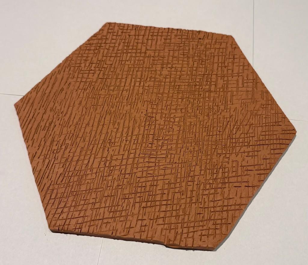 Bovenaanzicht: regelmatige hexagonale terracotta plaat met warm roodbruine kleur en fijne kruisgroefstructuur op het oppervlak